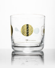 A Cognitive Surplus Atomic Models Whiskey Glass with a gold design on it.