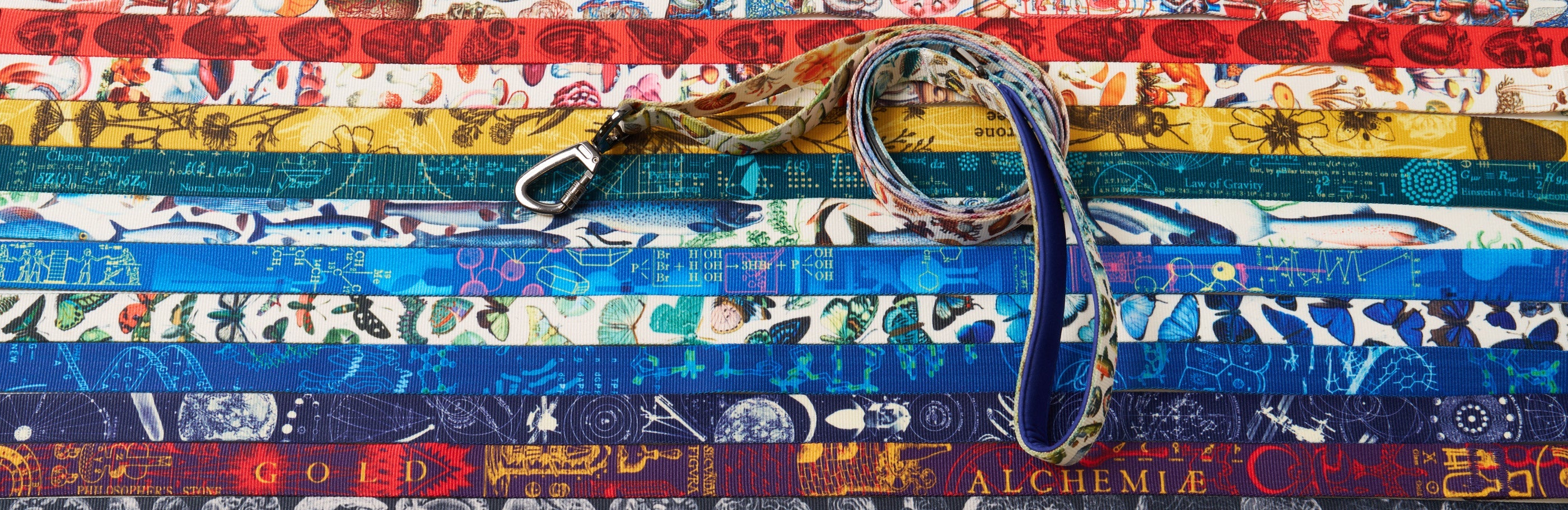 A coiled lanyard with a metal clip lies on top of several colorful, patterned lanyards arranged in parallel rows.