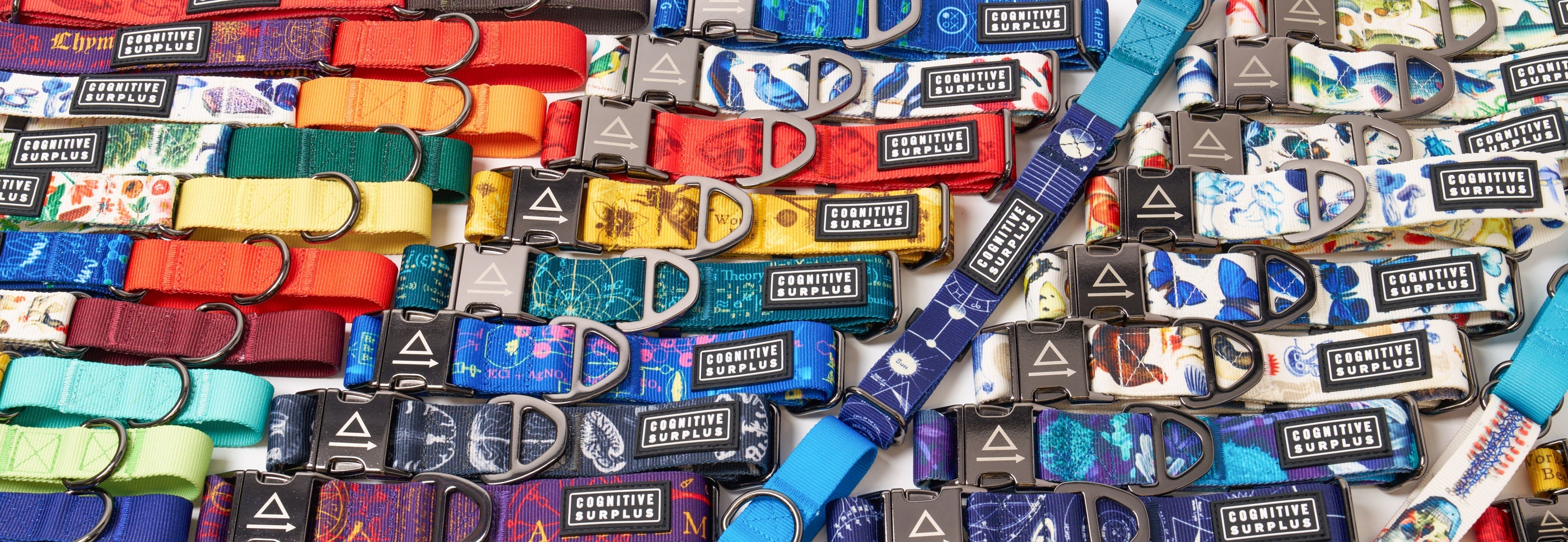 Three blue patterned dog collars of varying sizes are arranged on a white background; each collar features a metal clasp and branded patch.