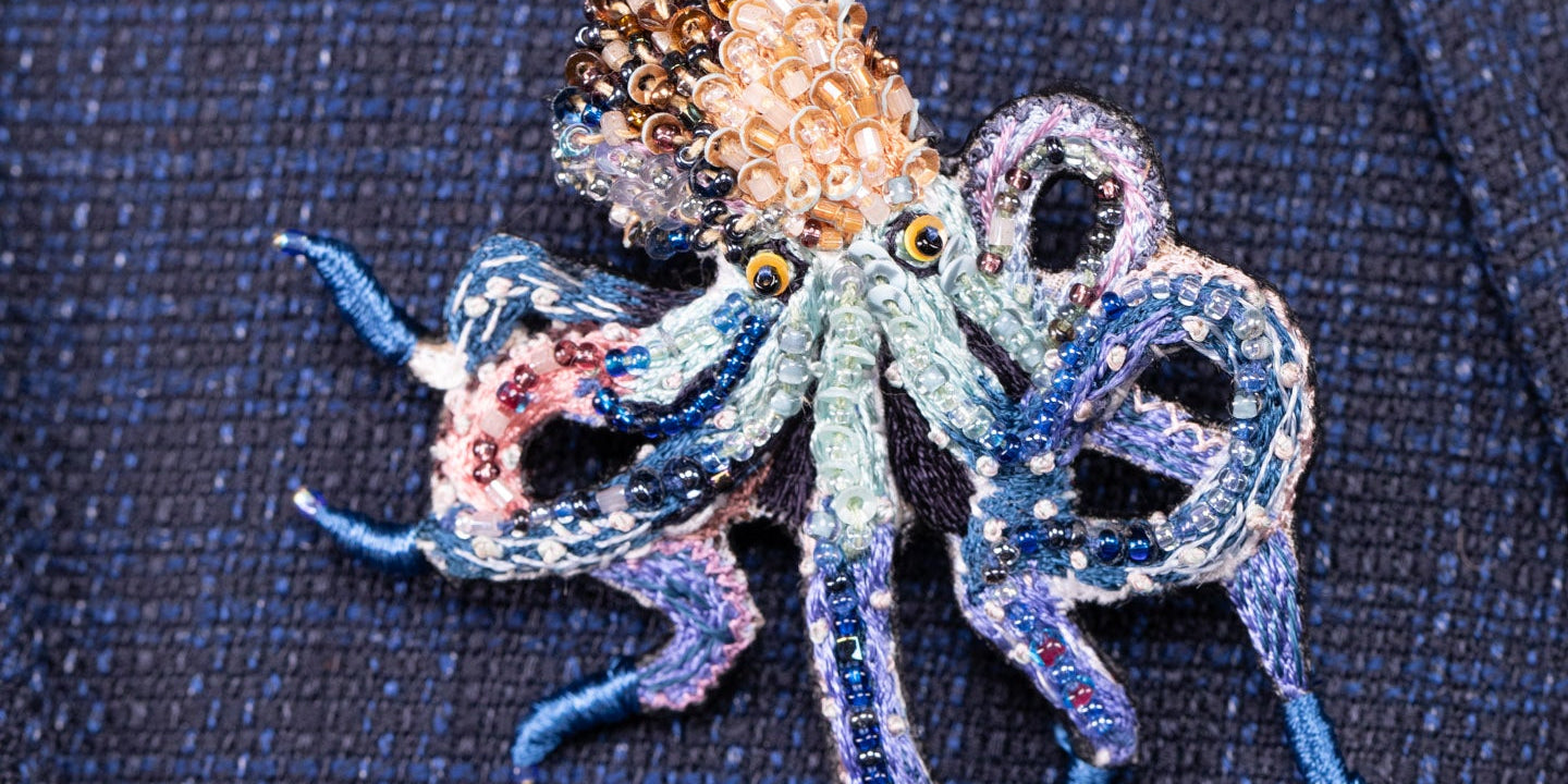 A beaded brooch shaped like an octopus is pinned to a textured dark blue fabric.