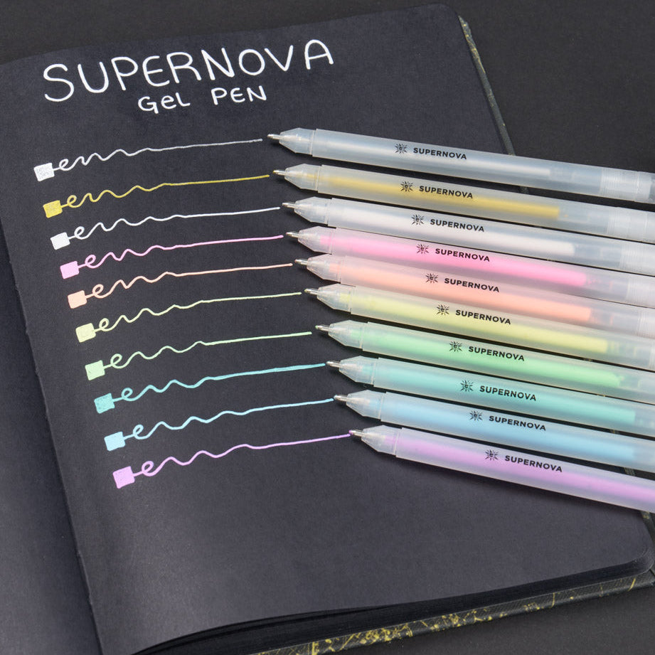 A black notebook shows nine gel pens labeled "SUPERNOVA," each drawing a colorful line. The lines display pastel colors on black paper, highlighting the pens' vibrant hues.