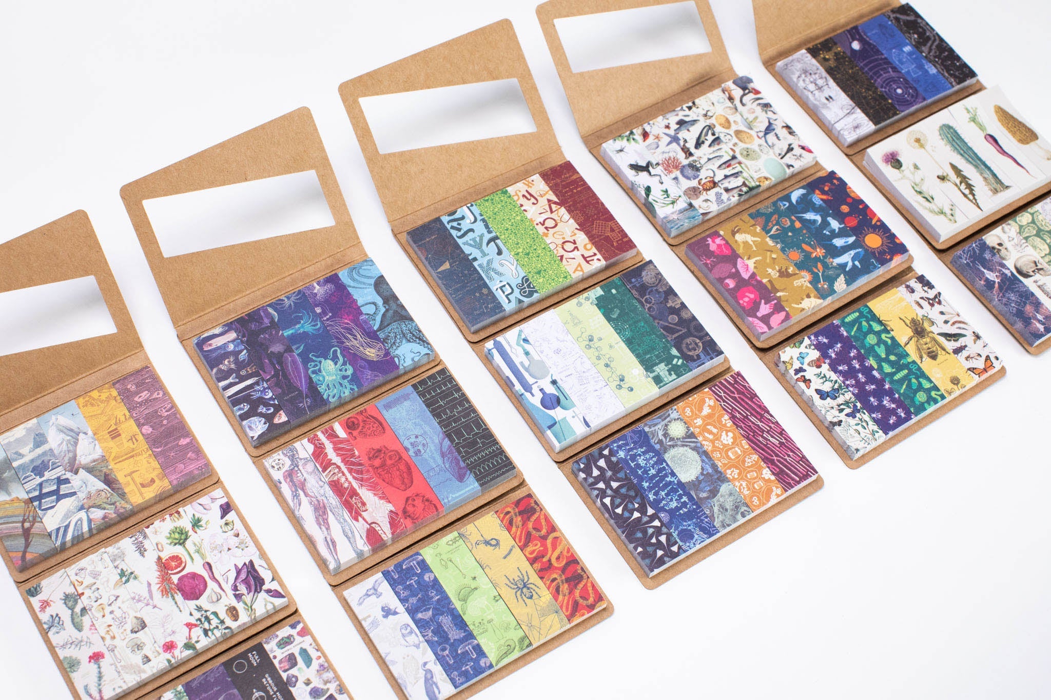 Sets of colorful decorative paper strips in various patterns and hues, displayed in open cardboard booklets on a white background.