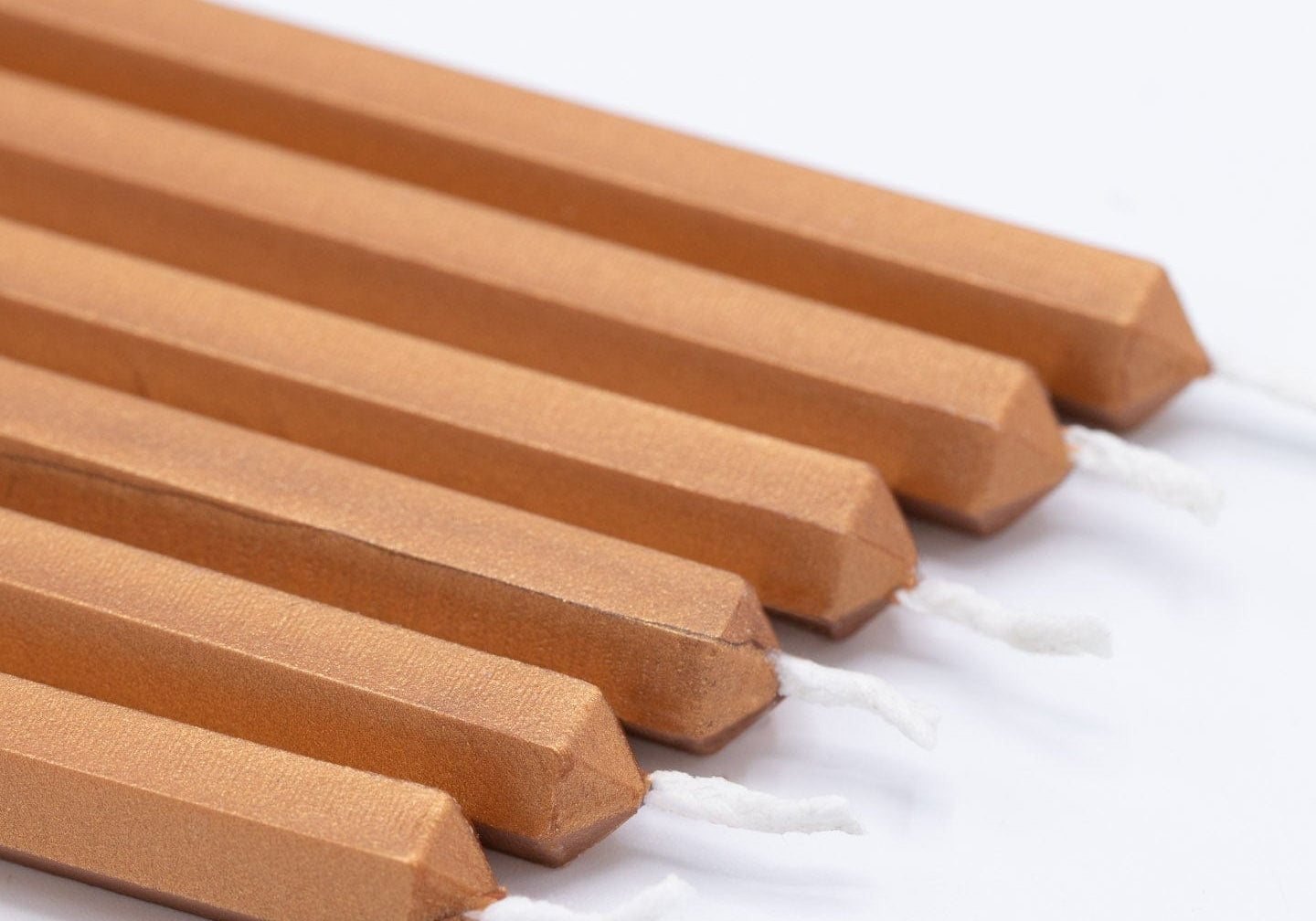 Six copper-colored candles with pointed ends, arranged in a row on a white background.