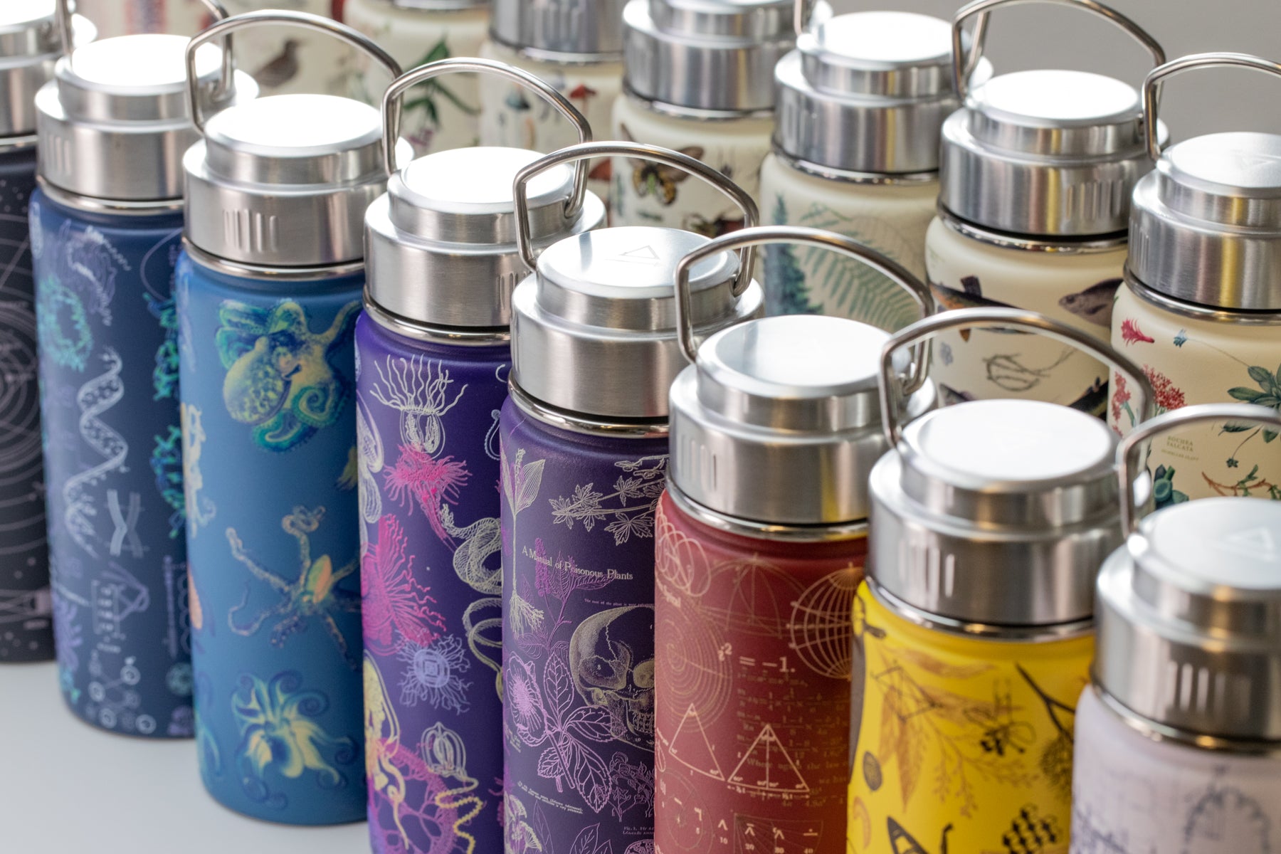 A collection of colorful reusable water bottles with various scientific and nature-inspired designs, arranged in rows.