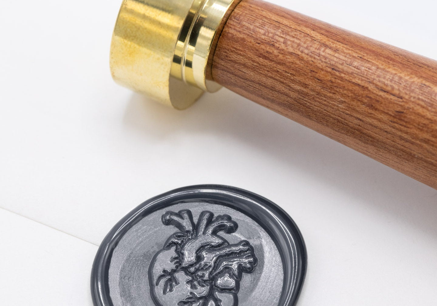 A wax seal with an anatomical heart impression, next to a wooden and brass stamp on white paper.