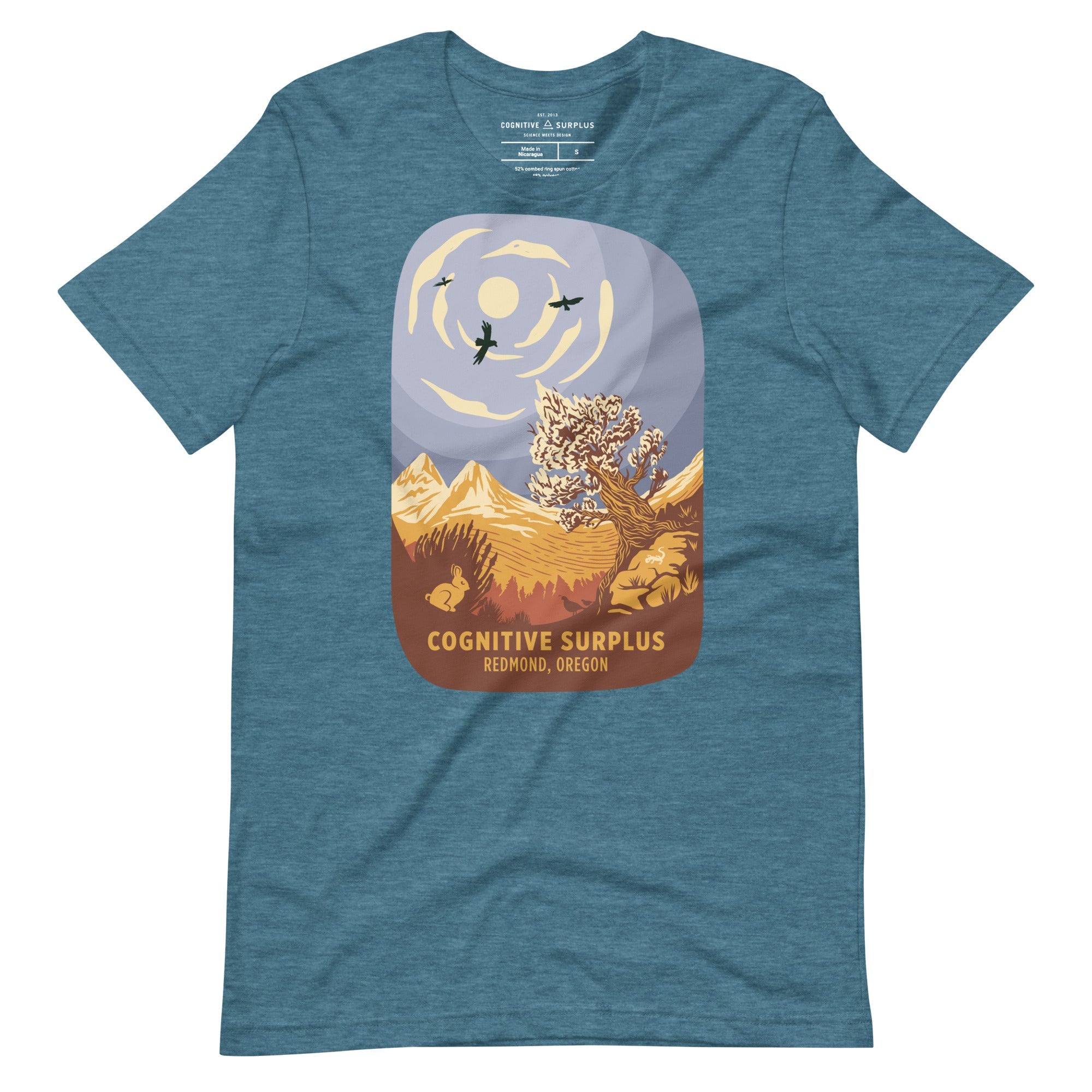 Blue T-shirt featuring an illustration of mountains, trees, birds, and the sun, with the text &quot;Cognitive Surplus, Redmond, Oregon.