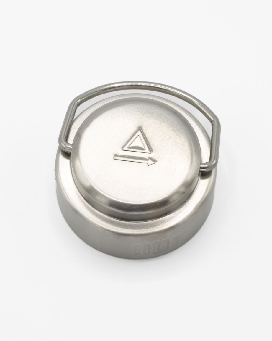 A Cognitive Surplus stainless steel lid with a triangle on it.