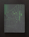 An image of the Spiders & Webs Dark Matter Notebook by Cognitive Surplus on a black background.