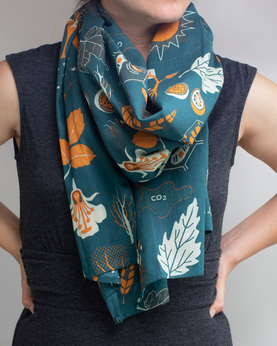 A woman wearing a Retro Botany Scarf by Cognitive Surplus with orange and green leaves.